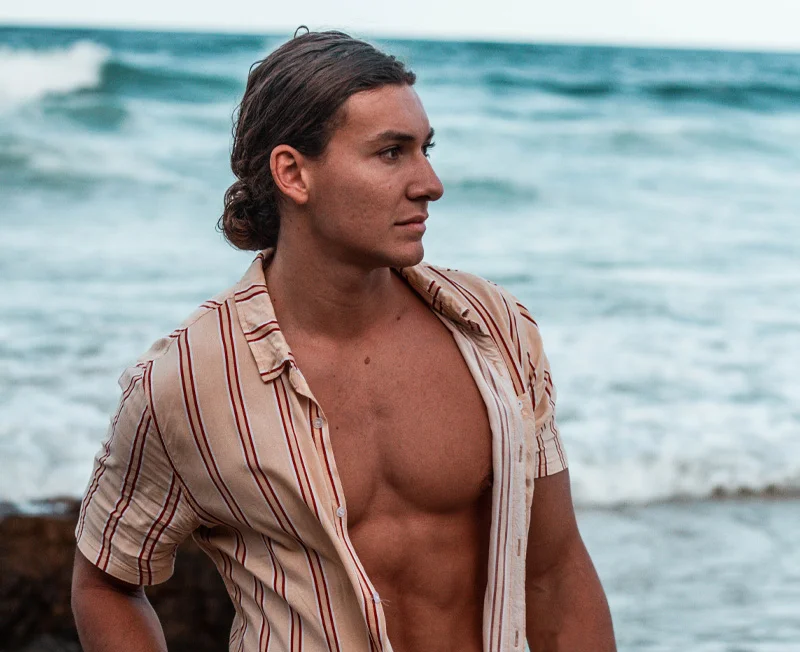 Man next to the ocean posing with his shirt unbuttoned