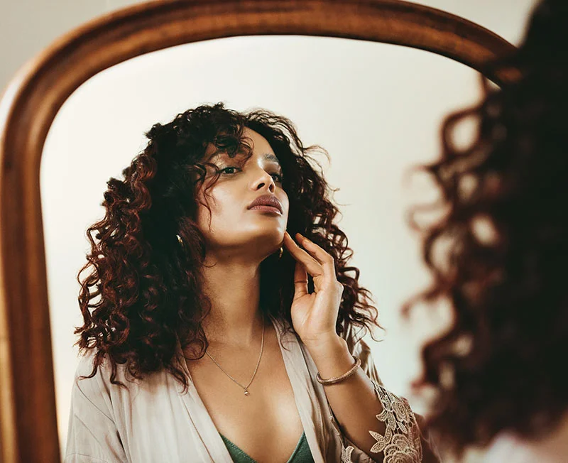 Curly haired woman looking at her skin in the mirror
